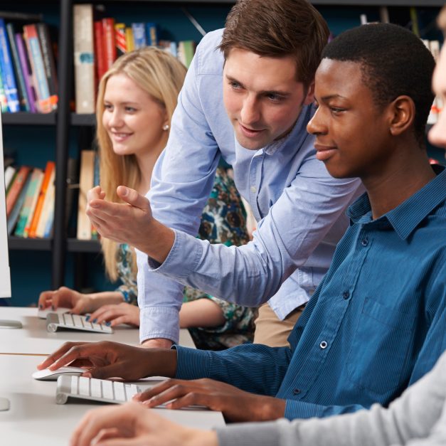 Tutor Working With Group Of Teenage Students Using Computers