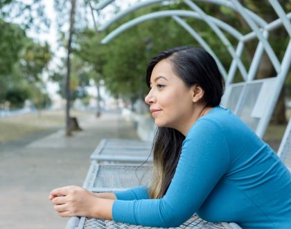 Woman sitting on a bench in the park with a thoughtful expression.